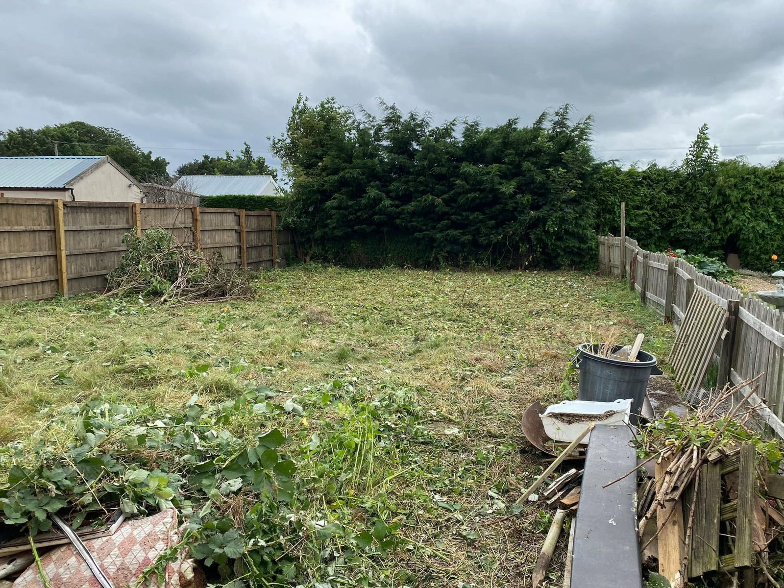 An overgrown back garden cut down and cleared, with the waste piled up