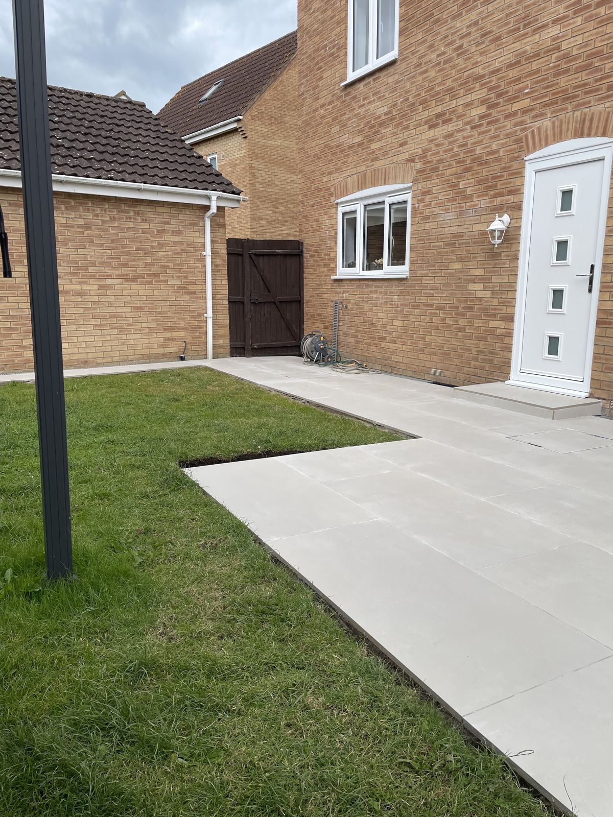 Light grey paving path running along a fresh lawn beside a modern brick house