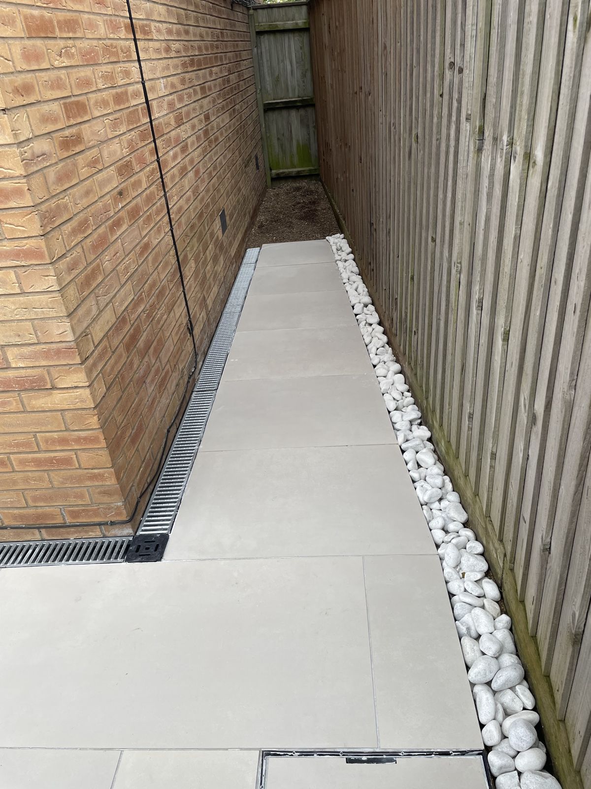 Narrow side return finished with light paving, a drainage channel and white pebbles